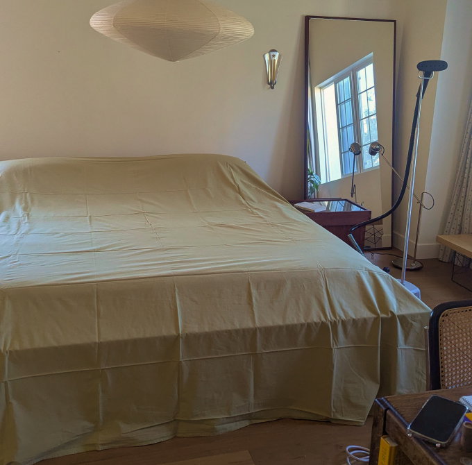 Wrinkled pale green sheet draped over a bed next to a steamer