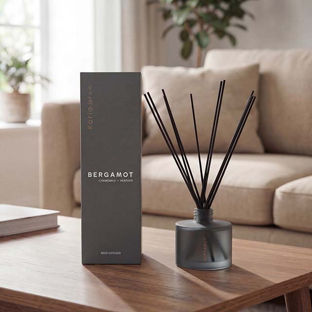 A Karla Bree reed diffuser labeled 'Bergamot' is on a table, with a modern living room setting in the background.