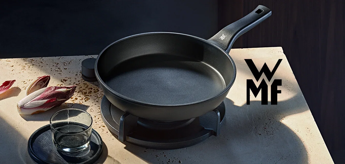 Schwarze Bratpfanne auf dem Herd mit gehackten Radicchio-Blättern, Glas Wasser auf einem Untersetzer und schwarzem Teller auf einer Steinarbeitsplatte.