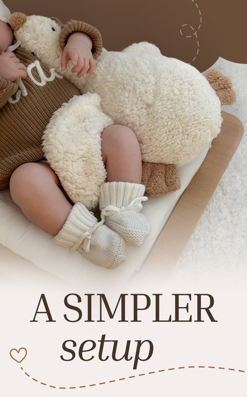 Baby resting on a cream plush duck toy with knit booties visible beside large text reading A Simpler Setup.