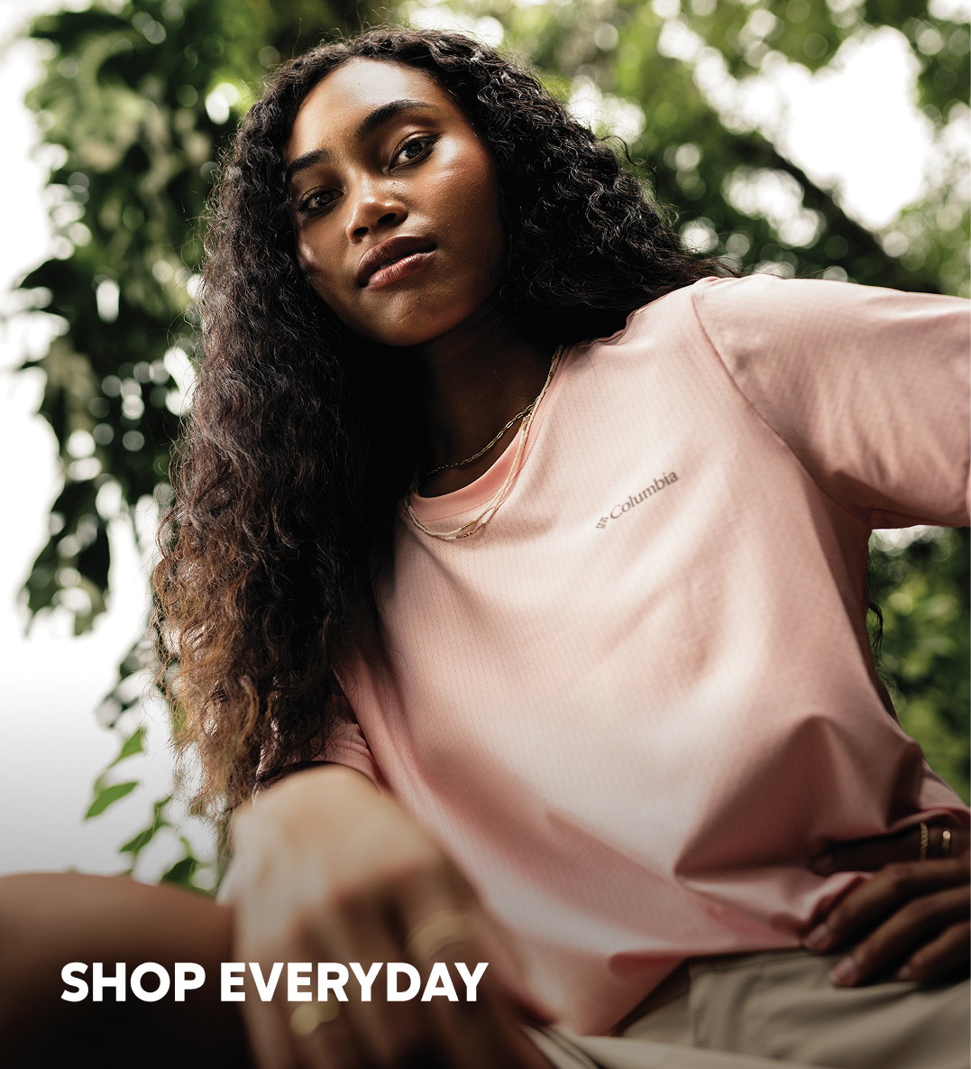 A woman wearing a pink short sleeve shirt and khaki shirts against green foliage with text: SHOP EVERDAY