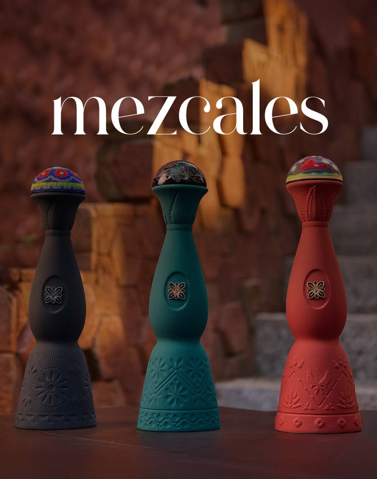 Three artisanal mezcal bottles (black, teal, red) with embroidered caps on stone steps, 'mezcales' logo above