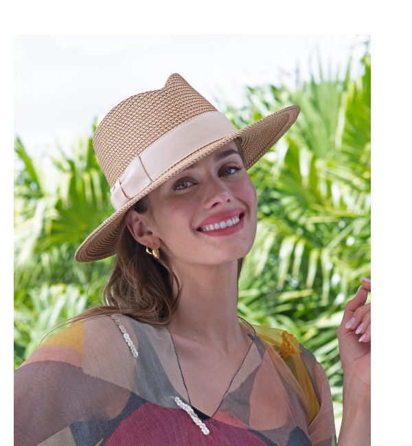 Woman wearing a straw hat and a colorful top, smiling against a backdrop of palm leaves.