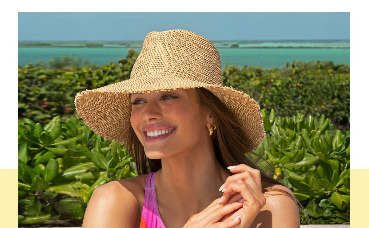 Woman smiling in a wide-brimmed hat with a scenic background of water and greenery.