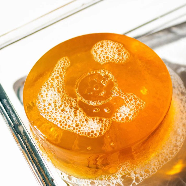 A round, translucent orange soap bar with a swirling pattern and bubbles on its surface sits in a sink. (square)