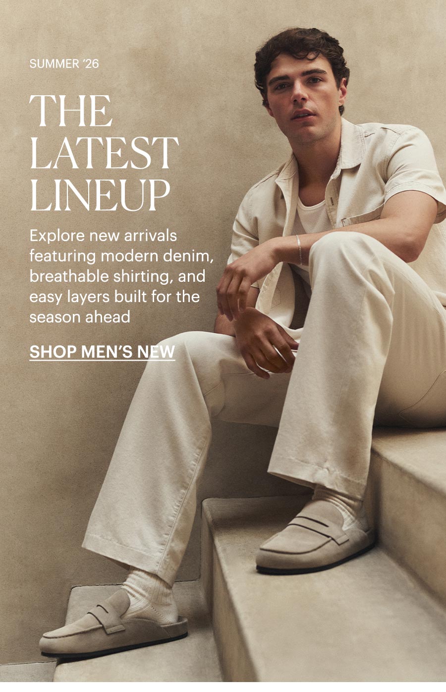 Man wearing a white denim short sleeve button-up over a white tee with matching white jeans and beige suede slip-on shoes, sat on a sunlit stone staircase. Summer '26: The Latest Lineup - Explore new arrivals featuring modern denim, breathable shirting, and easy layers built for the season ahead. Shop men's new arrivals.