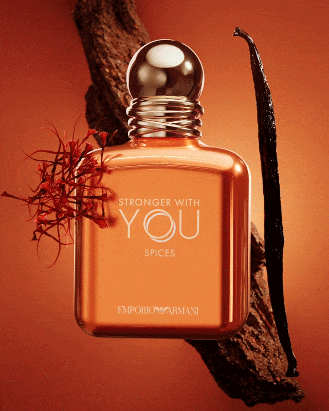 Frasco de perfume Emporio Armani "Stronger With You Spices" rodeado por una rama de madera, una vaina de vainilla y hebras de azafrán.