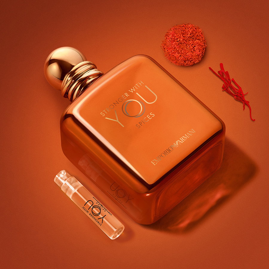 Frasco de perfume Emporio Armani "Stronger With You Spices" y muestra sobre un fondo naranja con azafrán y especias.