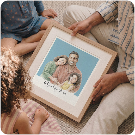 A family sitting together on the floor, looking at a framed watercolour illustration of a dad and child