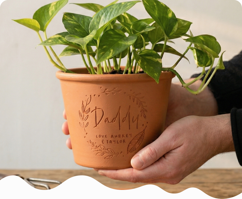 A pair of hands holding an engraved terracotta pot personalised with "Daddy, Love Amber & Taylor"