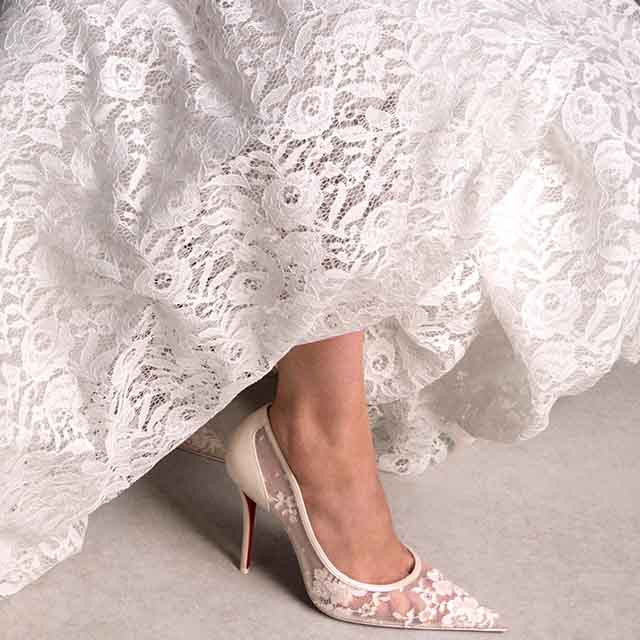 A close-up of a person wearing white lace shoes and a white lace dress.
