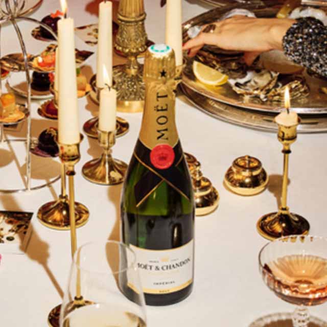 A bottle of Moët & Chandon champagne on a candlelit table with oysters and glasses.
