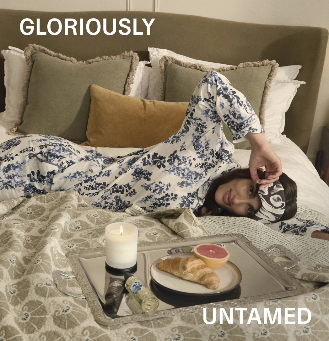 A woman lies on a bed with a face mask on next to a lit candle and some breakfast