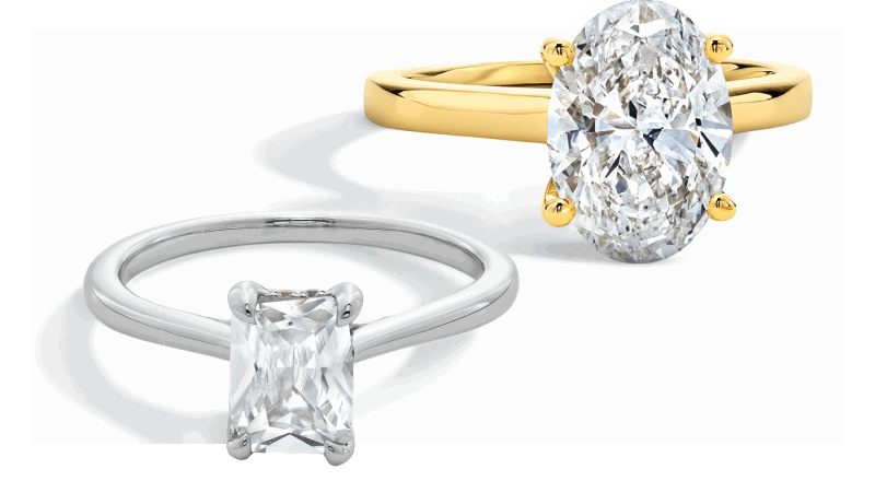 Two diamond engagement rings with oval and emerald-cut stones in yellow and white gold solitaire settings.