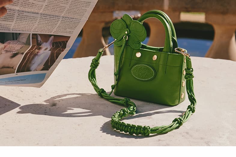 Olympia tote mini on table with orchid accessory with knotted long strap in dill gold. 