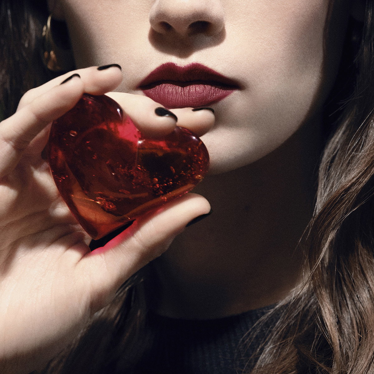 A model with red lipstick holds a translucent red glass heart.