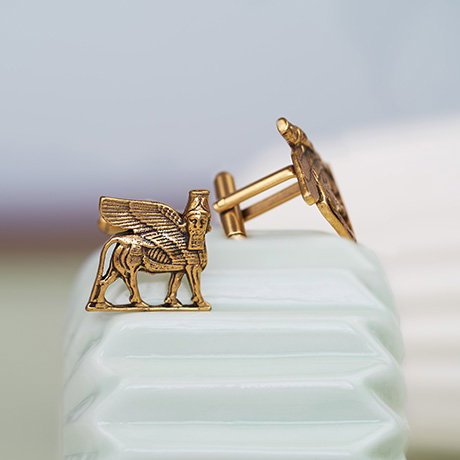 Pair of brass cufflinks featuring ancient Assyrian lamassu, propped on a pastel ceramic shape. - Shop Jewellery.