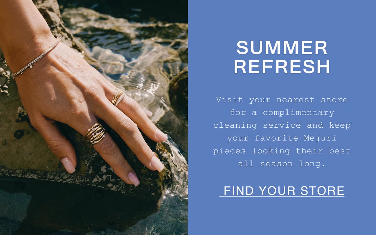 A close-up of a hand resting on a wet rock, wearing a gold multi-band ring, a gold ridged statement ring, and a delicate diamond tennis bracelet. Beside the image, text on a periwinkle blue background reads "Summer Refresh — Visit your nearest store for a complimentary cleaning service and keep your favorite Mejuri pieces looking their best all season long." with a "Find Your Store" call-to-action link.