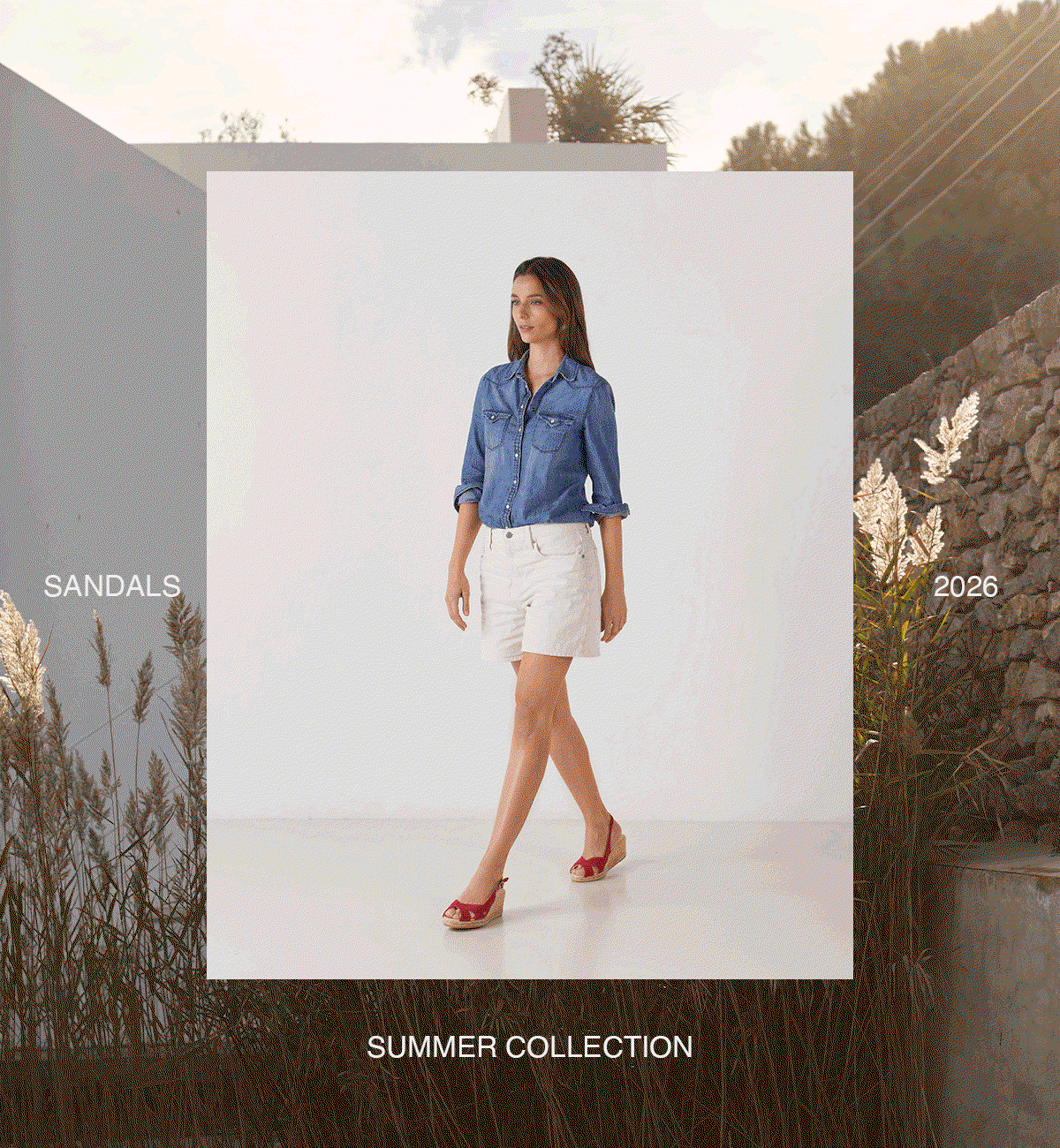 Woman in a denim shirt and white shorts walking in red espadrille sandals, framed against a sunlit outdoor landscape with the text “Sandals 2026 Summer Collection.”