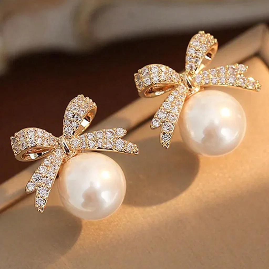 Pearl Accessories: Gold bow earrings with white pearls and cubic zirconia crystals on model's ear