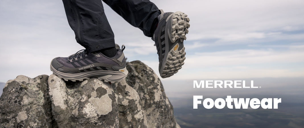 Model wearing Merrell walking shoes steps on a mossy rock.