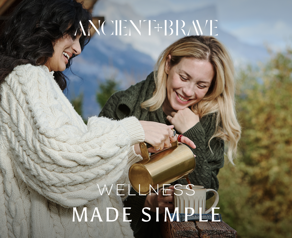 Two women sharing Ancient + Brave drinks, with a scenic mountain backdrop and the overlaid text 'Wellness made simple'.