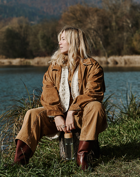 A woman sitting in a in front of a lake, holding a water bottle.