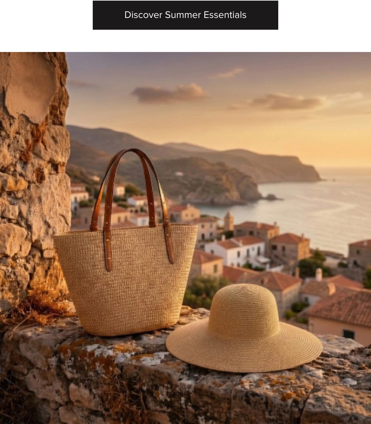 A straw bag and a wide-brimmed hat on a stone wall with a coastal village in the background at sunset.