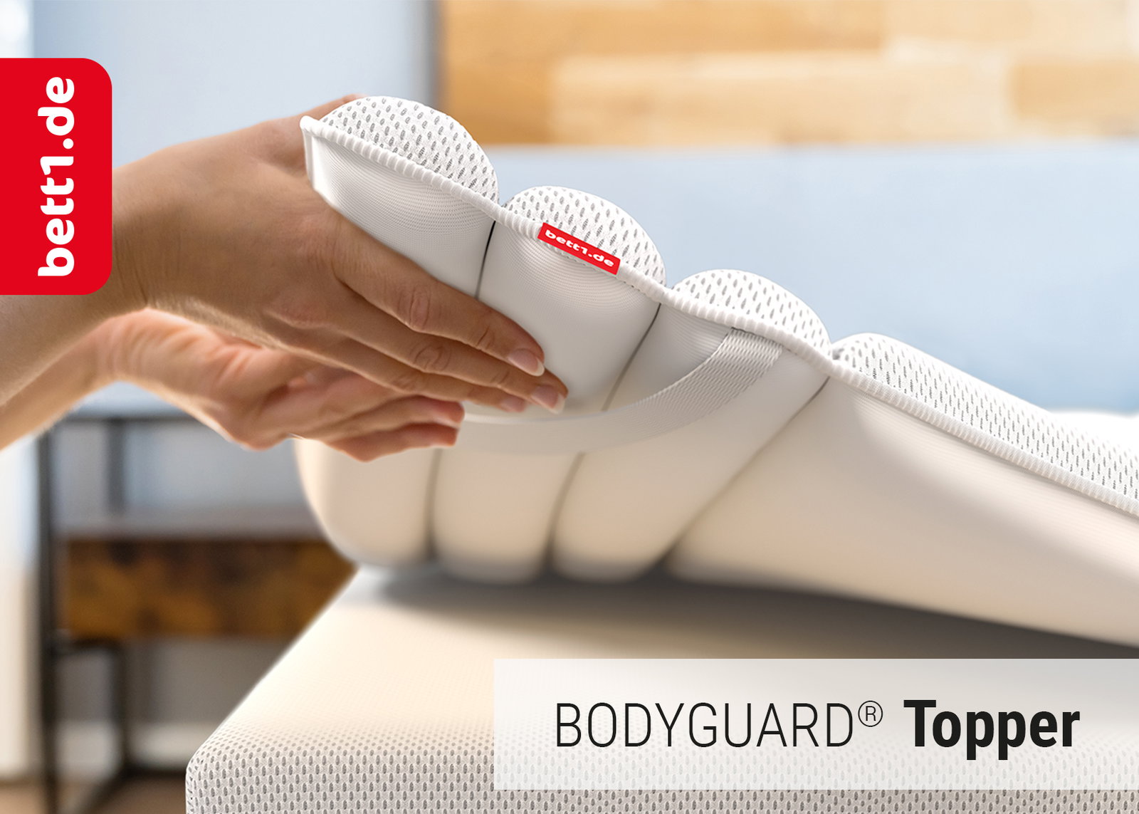 Foto: Hände legen einen BODYGUARD Topper auf eine BODYGUARD Matratze.