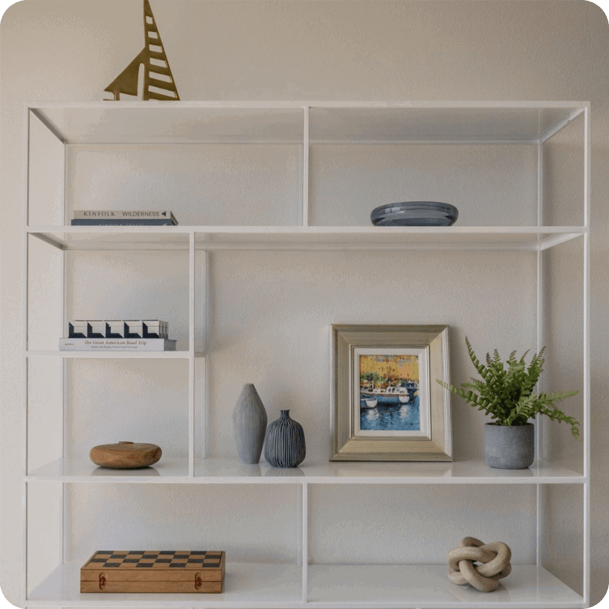 White Foshay bookcase with open shelves holding books, framed art and small decor objects.