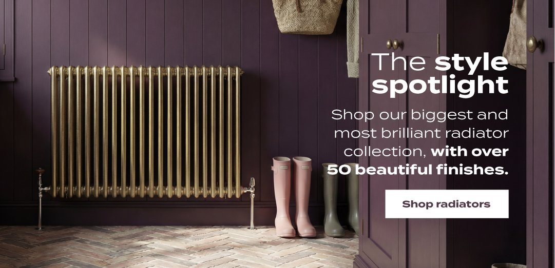 Traditional gold horizontal radiator against dark purple panelled walls with boots and herringbone wood flooring in a luxury hallway interior