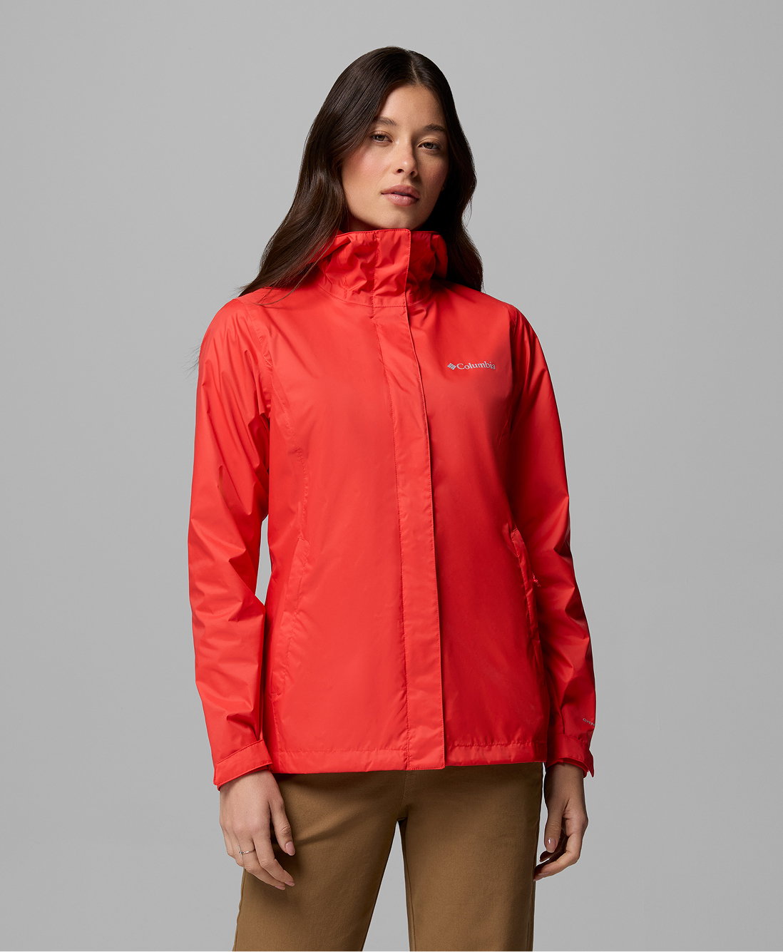 A woman wearing a red rain jacket and brown pants against a grey background.