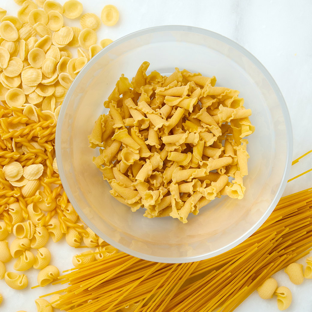 A deep Anyday dish filled with pasta, surrounded by various dried pasta shapes.