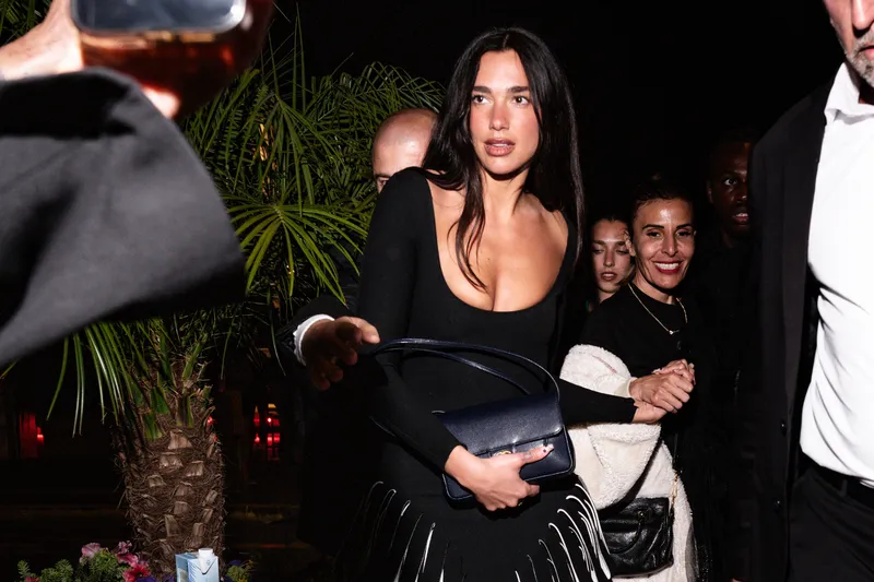 Image may contain: Dua Lipa, Adult, Person, Accessories, Bag, Handbag, Clothing, Dress, Photobombing, Formal Wear, and Suit