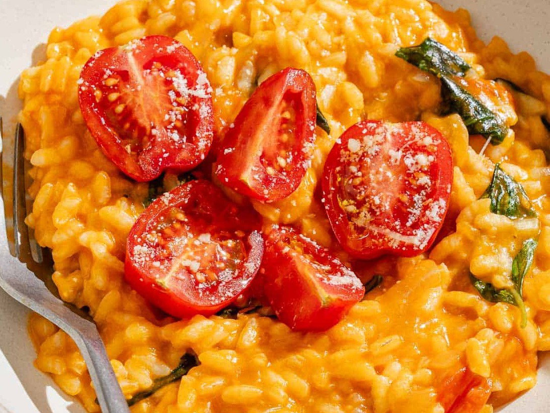 Tomato risotto topped with tomatoes in a bowl with a fork.