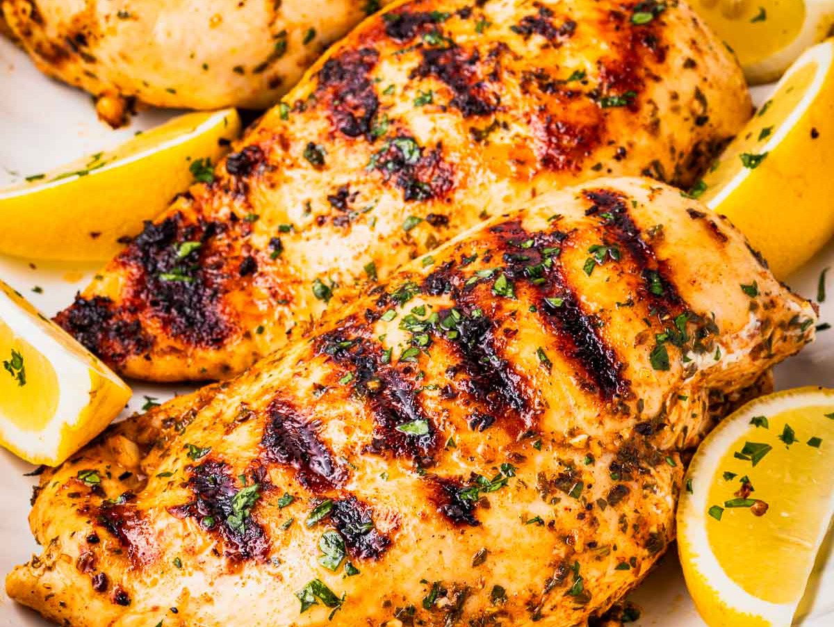 Greek marinaded chicken on a platter with lemon wedges.