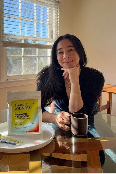 Meagan Kong sitting at her kitchen table drinking coffee mixed with Advanced 4-In-1 Boost. Shop now. 