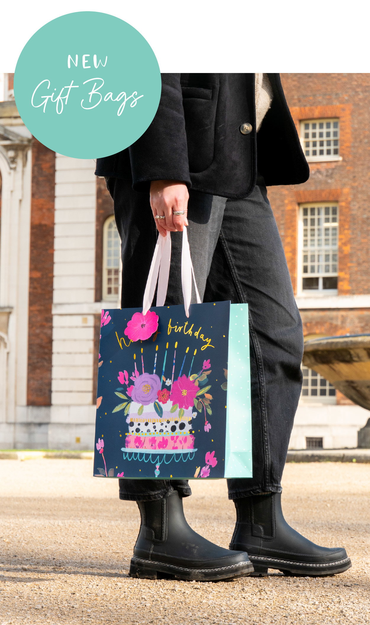 Striped pastel gift bag held outdoors in spring sunshine with pink ribbon handles
