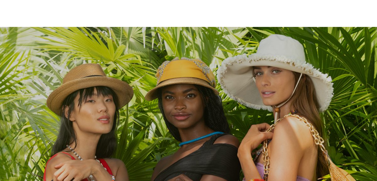 Three women wearing stylish hats, surrounded by lush green foliage.