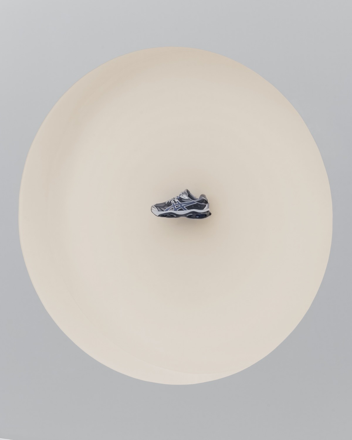 Grey running trainer centred on a large pale beige circular backdrop against a light grey studio background