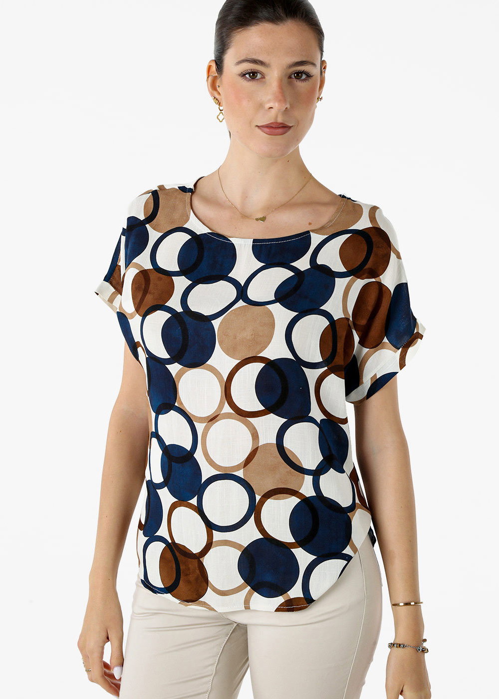 Woman modelling short-sleeve blouse with navy and brown circular print, cream trousers and minimal jewellery on white background