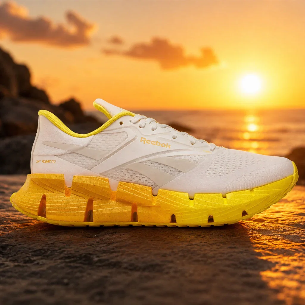 White and yellow Reebok running shoe with FloatZig technology displayed on a beach at sunset.