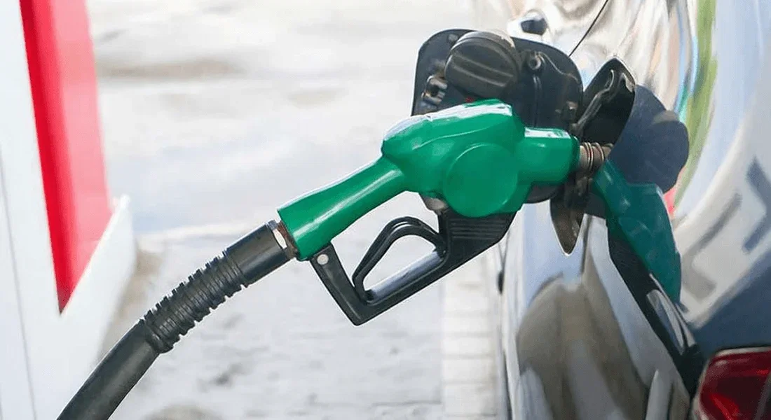 A green fuel pump nozzle inserted into a car at a petrol station.