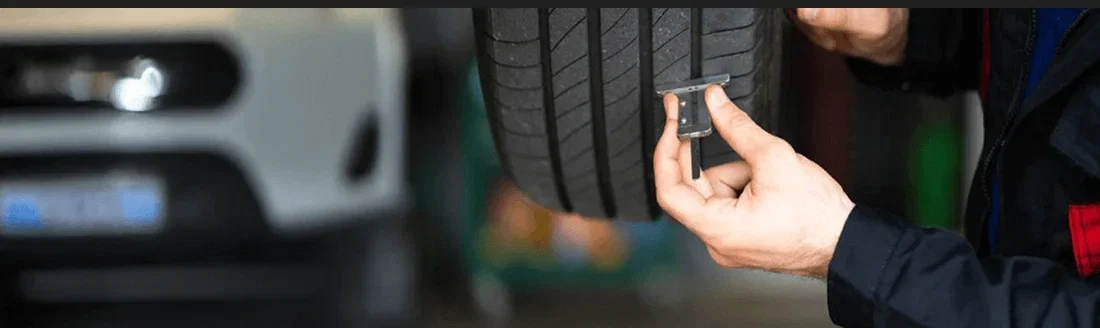 A mechanic checking tyre tread depth with a gauge.