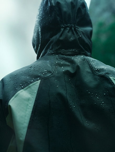 Close-up of a green jacket with water running off the surface, highlighting its waterproof material.