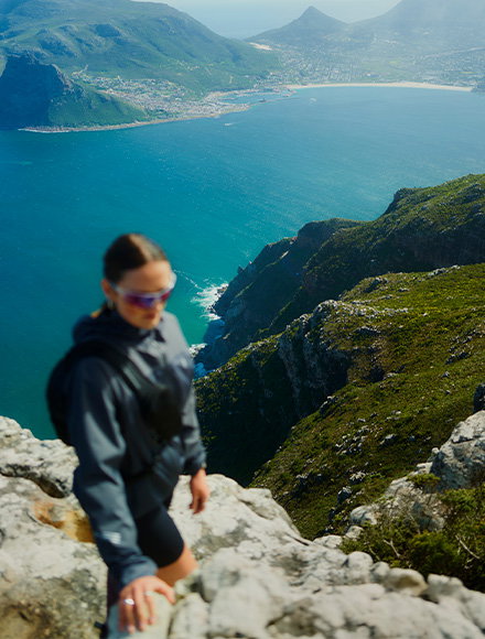 A woman hiking in the mountains, with water and distant peaks visible in the background.