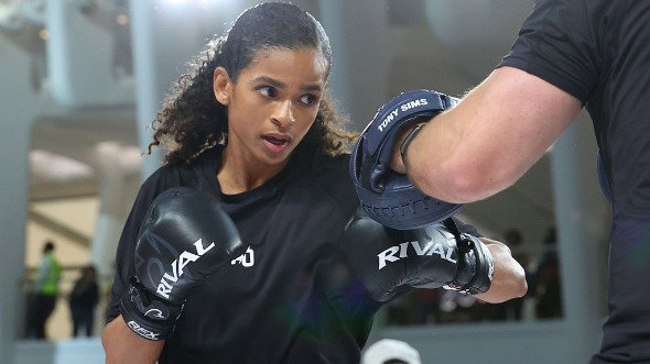 Boxer Ramla Ali, a woman with long curly hair and wearing black boxing gloves, trains with her coach.