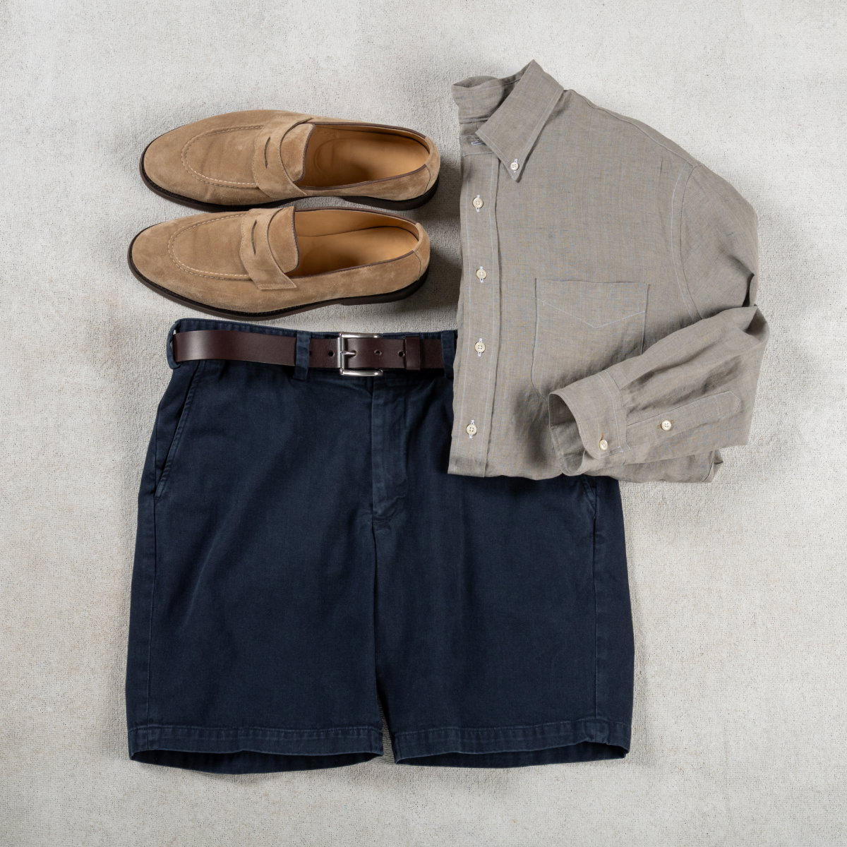 A pair of navy Bills Khakis Heritage Wash shorts sit with a grey Bills Standard fit shirt and loafers
