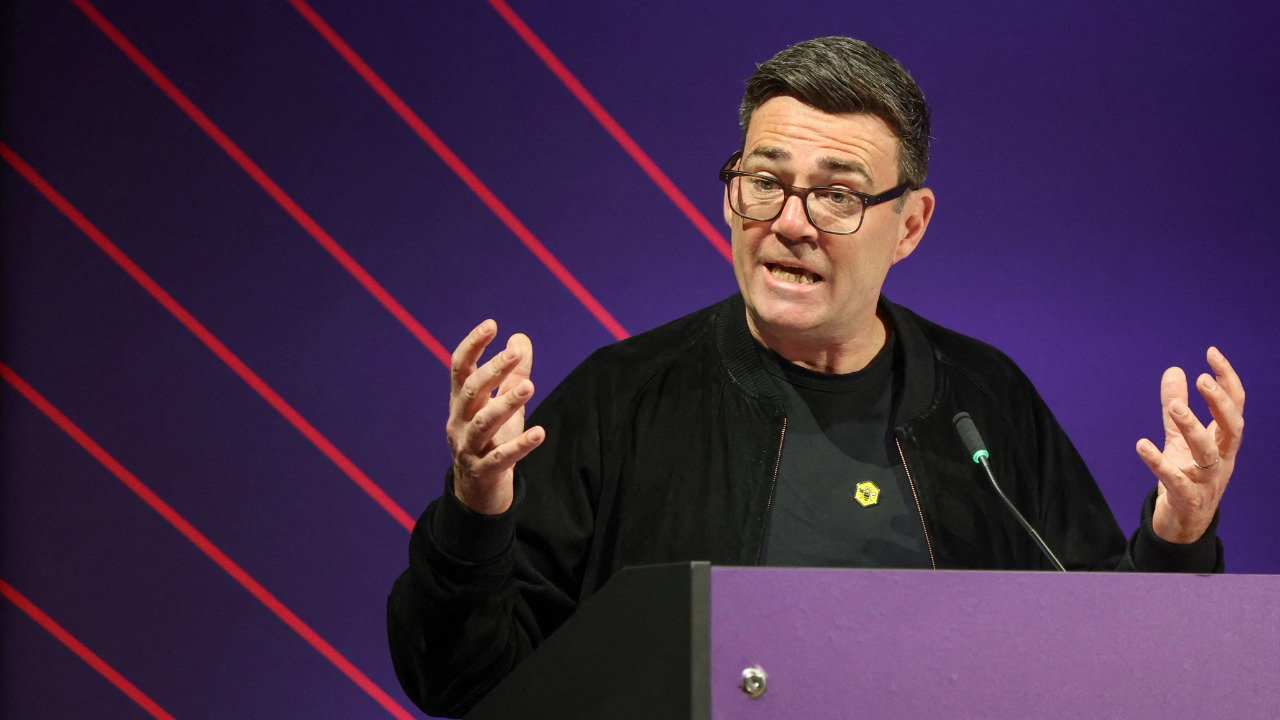 Greater Manchester Mayor Andy Burnham delivers a speech on 'Powering and Connecting the North' at The Great North Investment Summit, in Leeds, Britain, May 18, 2026. He wears a dark jacket, dark t shirt and glasses. He has short, dark hair.