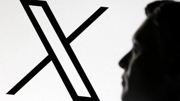 A 3D-printed miniature model of Elon Musk's head looks at a background showing the black and white X logo.